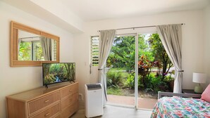 A bedroom with a bed, a TV, a dresser, and a sliding glass door leading to a garden.