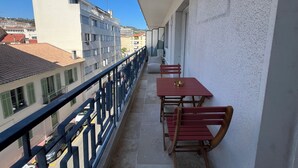 Un balcón con mesa y sillas, barandilla y vistas a edificios en el fondo.