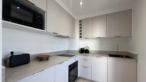 Una cocina moderna con armarios blancos, un microondas negro, un hervidor y una tostadora.