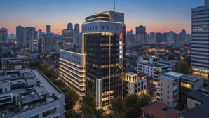 Een modern hotel met een opvallend verticaal bord, omringd door andere gebouwen in een stadsgezicht.