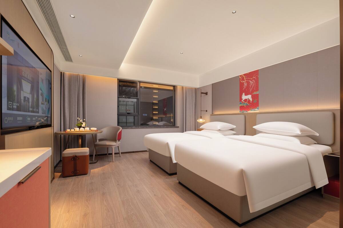 A hotel room with a bed, a desk, a chair, a window, and a TV screen.