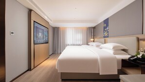 Een hotelkamer met een groot bed, een nachtkastje met een lamp, een tv aan de muur en een raam met gordijnen.