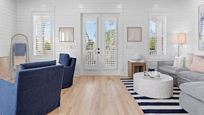 A modern living room with a wooden ceiling, white walls, and a large window with blinds. There are two blue armchairs, a grey sofa, and a round coffee table. - Reel McCoy, Seagrove Home with Hot Tub & Fire Pit (Santa Rosa Beach)