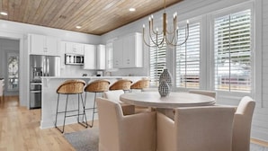A modern kitchen with white cabinets, a stainless steel refrigerator, and a dining area with a round table and four chairs. - Reel McCoy, Seagrove Home with Hot Tub & Fire Pit (Santa Rosa Beach)