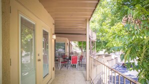 A covered balcony with a table and chairs, a door with a glass panel, and a view of the street and parked cars.