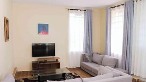 A living room with a flat-screen TV, a grey sofa, and a coffee table. - Lux Suites Boffar Residence Naivasha (Naivasha)