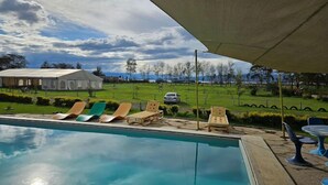 A swimming pool with lounge chairs and a table under a canopy, overlooking a grassy area with a building in the background. - Lux Suites Boffar Residence Naivasha (Naivasha)