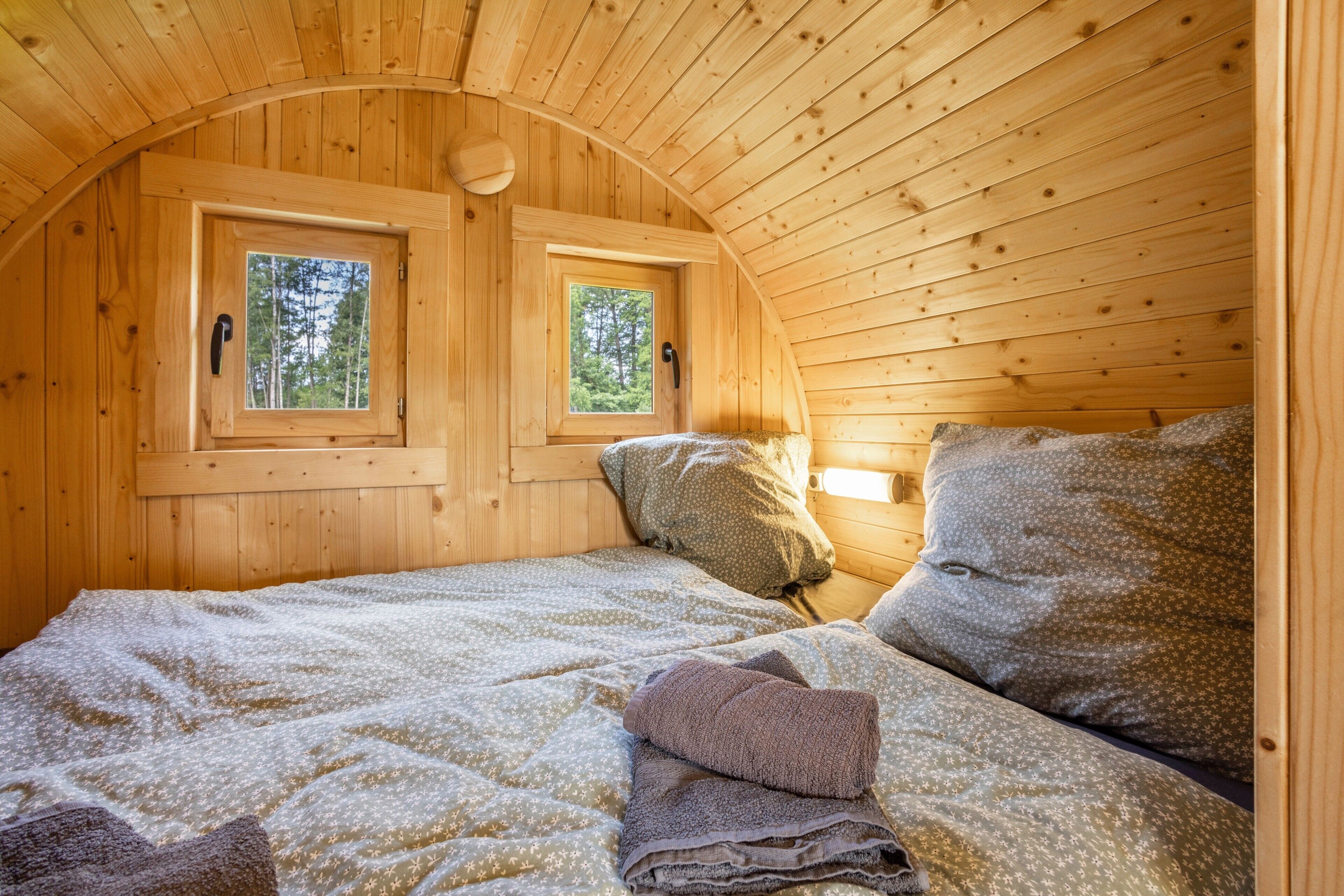A cozy wooden cabin room with a bed, two windows, and a curved ceiling.