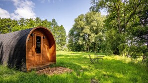 Eine Holzhütte mit gewölbtem Dach in einer grasbewachsenen Umgebung mit Bäumen.