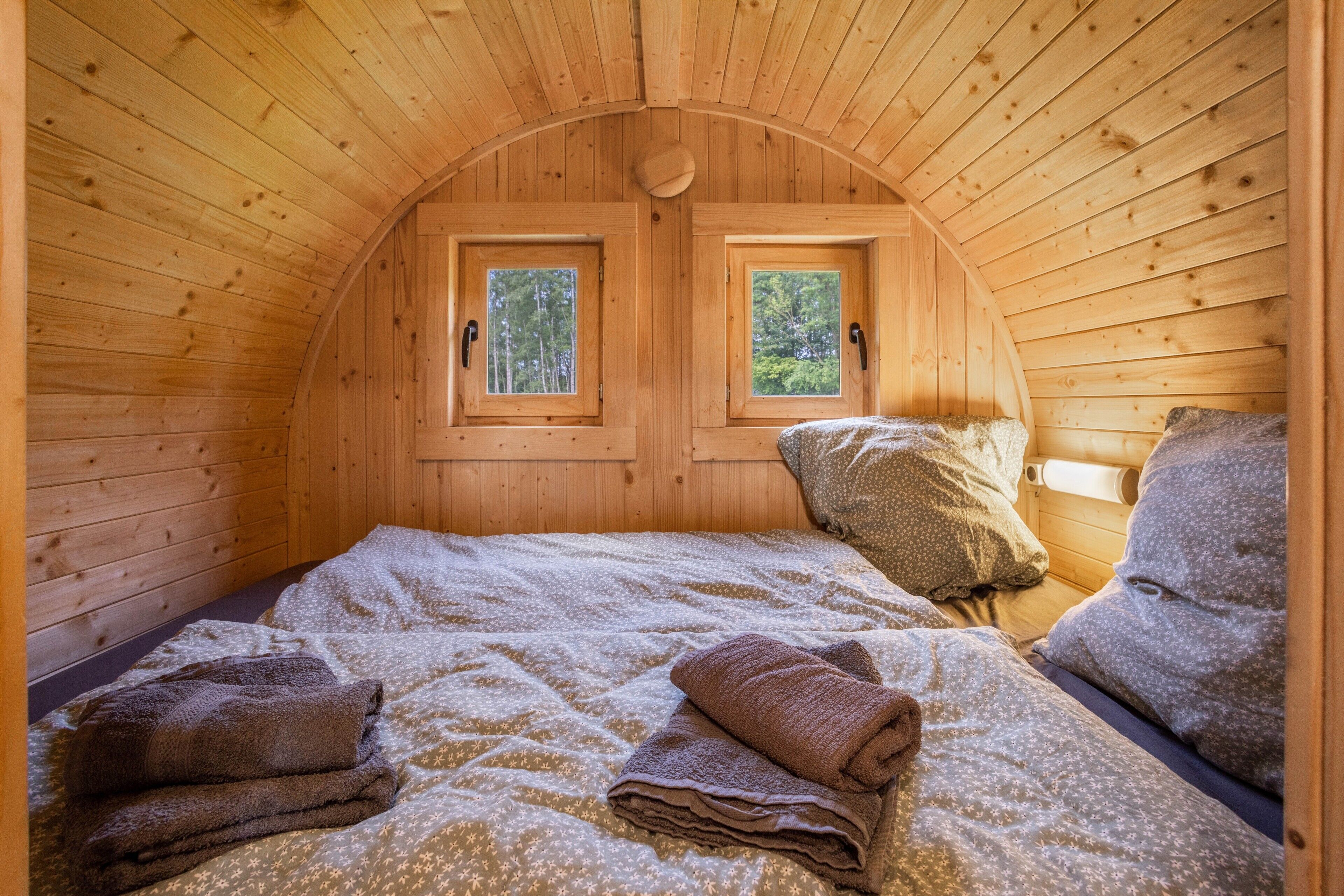 A cozy wooden cabin room with two windows, a bed with a patterned bedspread, and a small table with a lamp.
