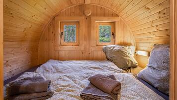 A cozy wooden cabin room with two windows, a bed with a patterned bedspread, and a small table with a lamp.