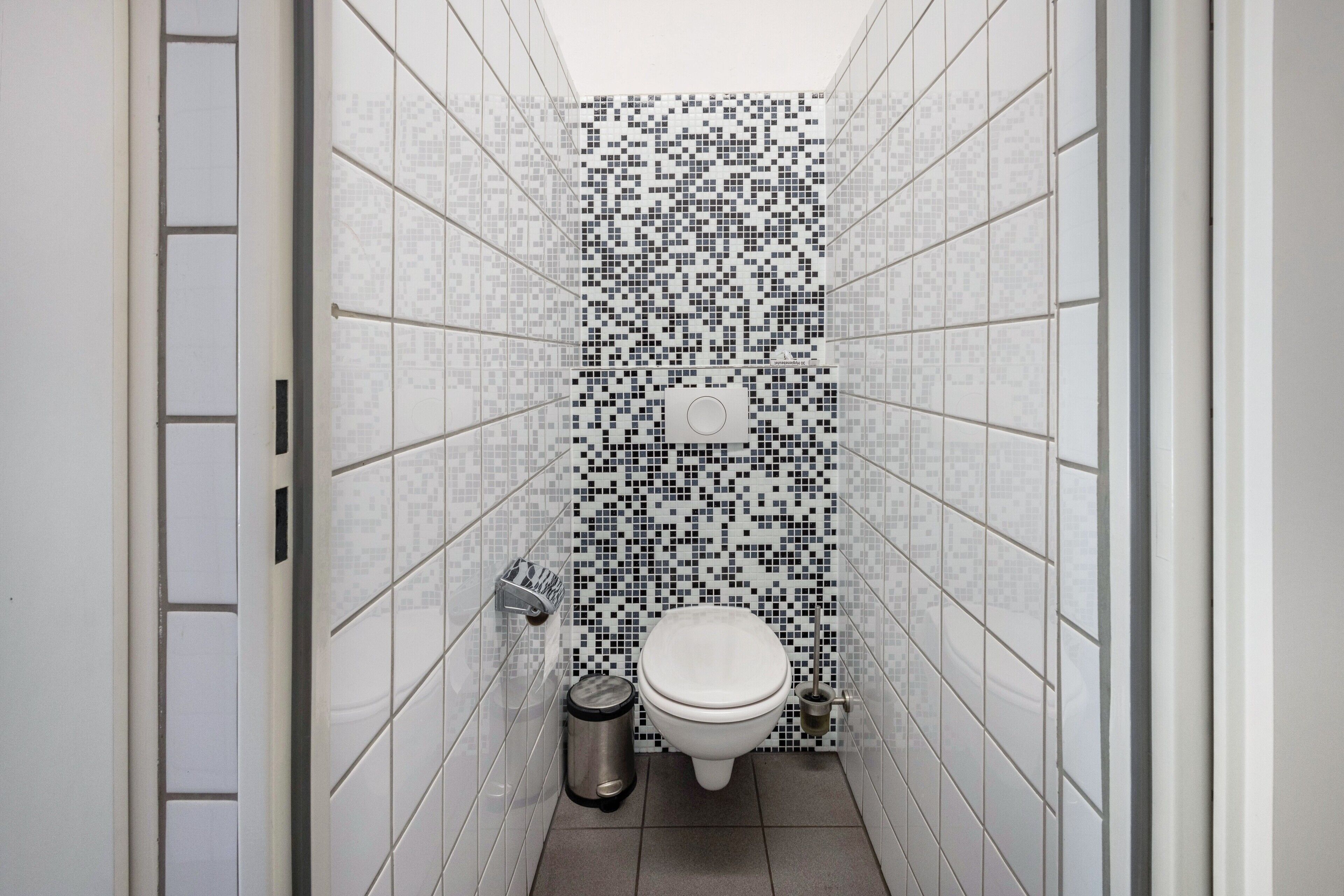 Une petite salle de bain avec un mur carrelé, des toilettes, une poubelle et un sèche-mains.