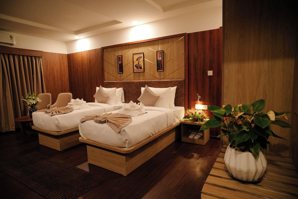 A hotel room with two beds, a wooden headboard, a nightstand with a lamp, a potted plant, and a mirror.