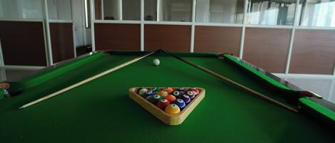 Une table de billard avec un triangle de billes, un queue et une bille blanche posées sur un tapis vert.
