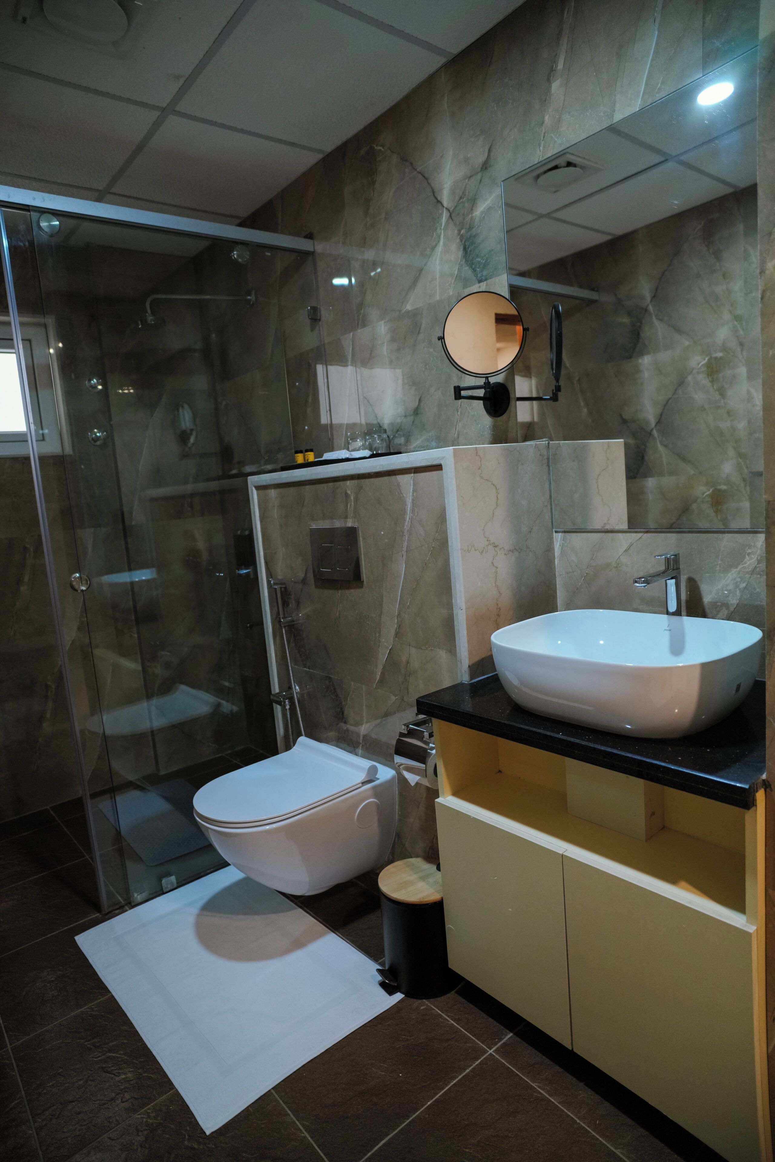 Une salle de bain moderne avec une douche à parois de verre, des toilettes blanches, un lavabo avec un miroir et un mur en marbre.