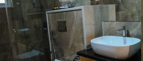 Une salle de bain moderne avec une douche à parois de verre, des toilettes blanches, un lavabo avec un miroir et un mur en marbre.