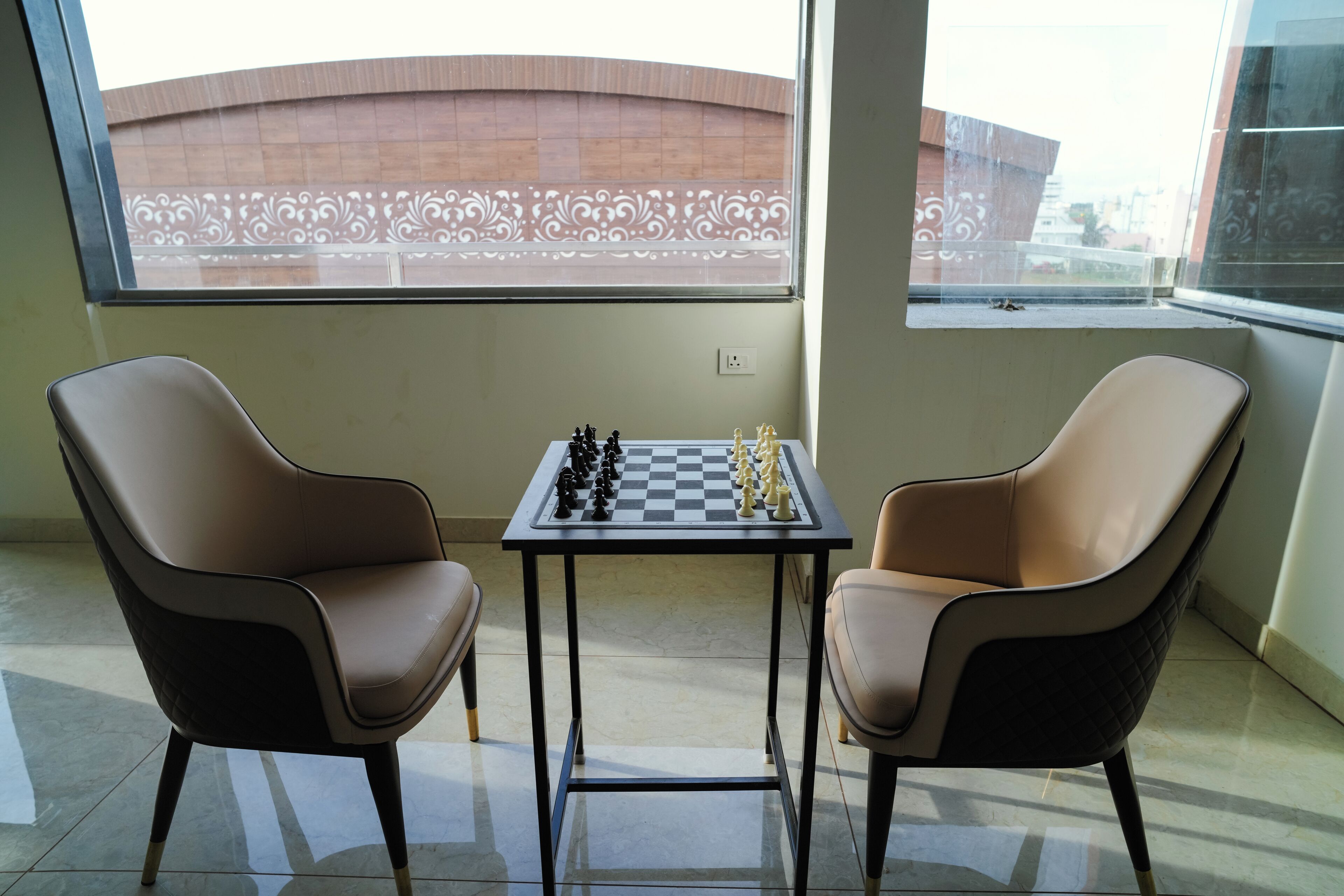 A room with two chairs facing a chessboard, a window with a decorative view, and a tiled floor.