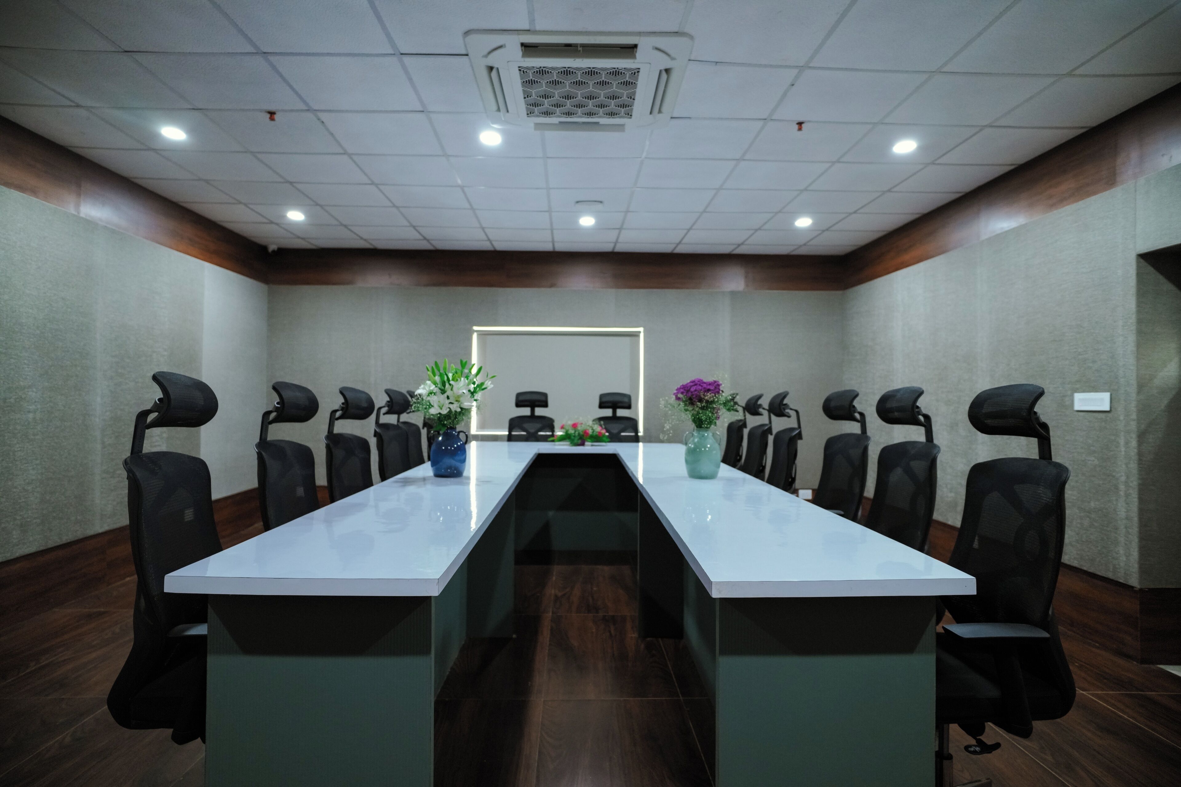 A conference room with a long table, black chairs, and two vases with flowers.