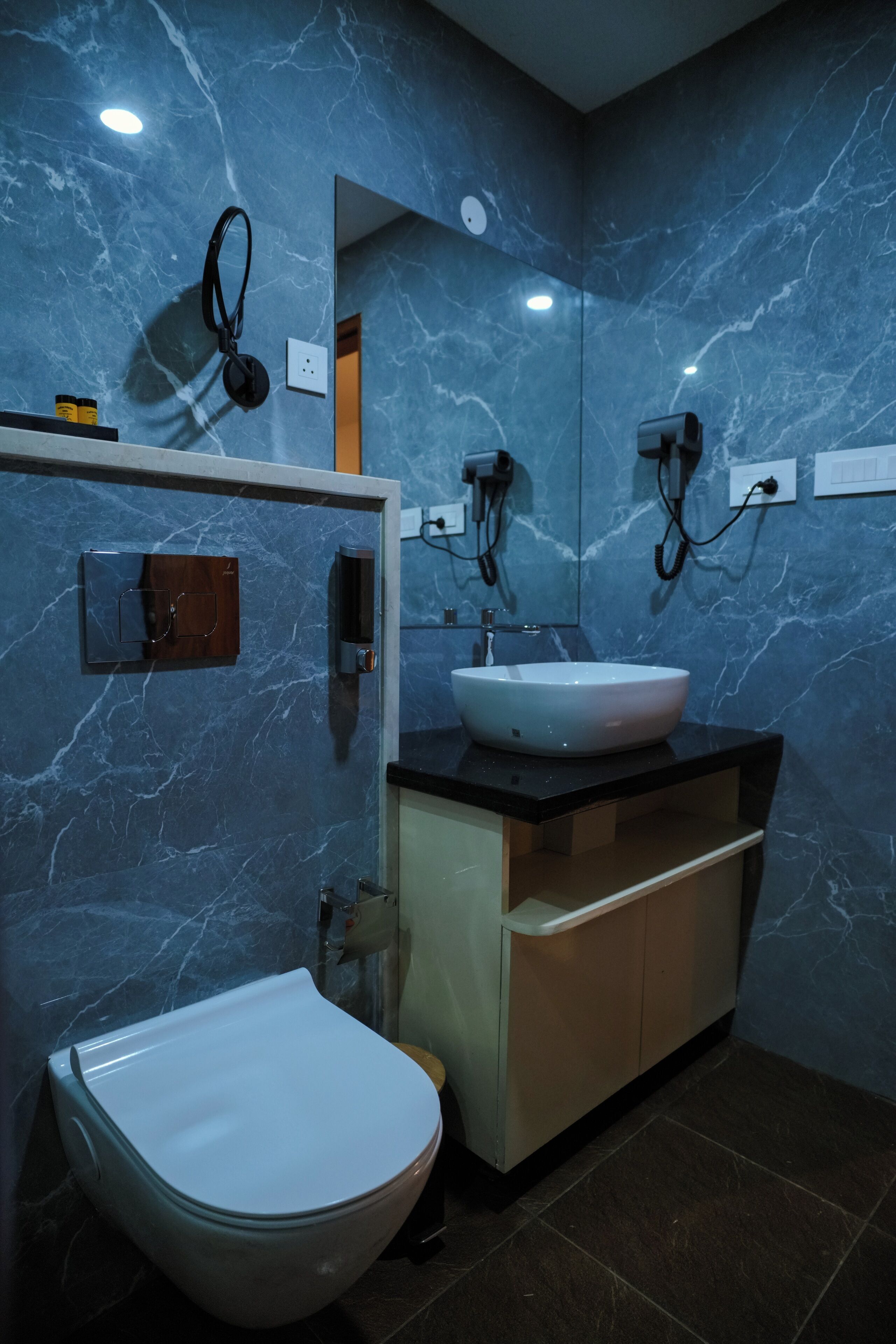 Un baño con inodoro blanco, un lavabo con espejo arriba y pared de mármol.