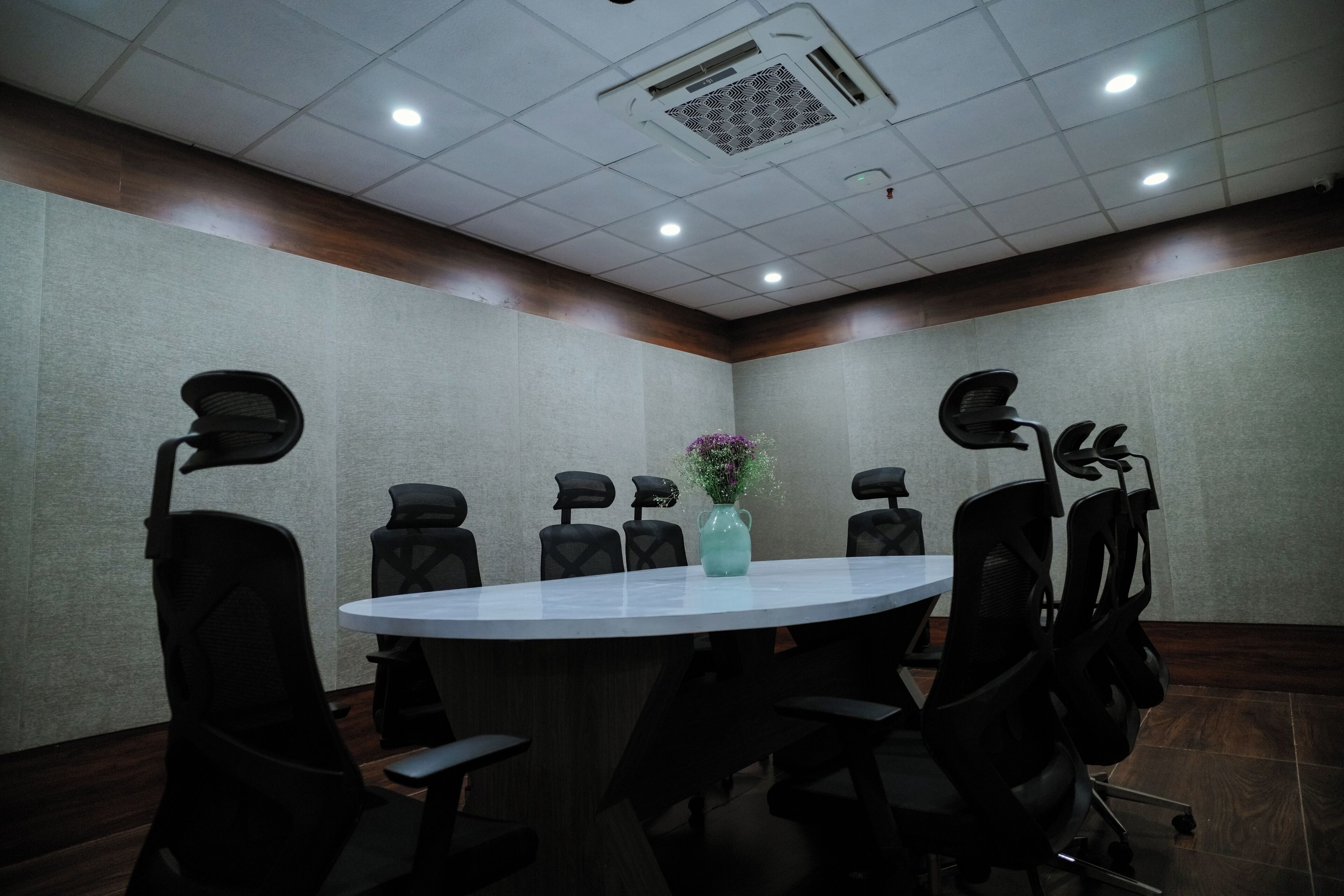 Una sala de conferencias con una mesa redonda, seis sillas negras y un jarrón con flores.