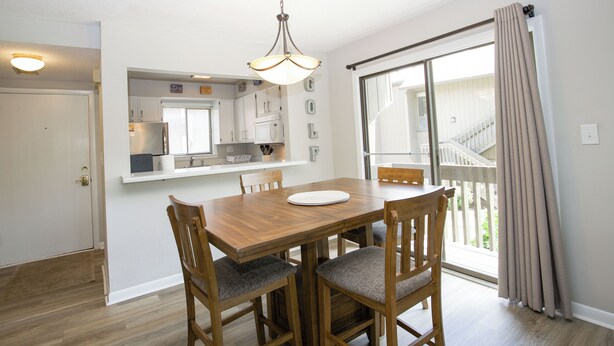 A dining area with a wooden table and chairs, a hanging light fixture, and a view of a balcony through a sliding glass door. - Cradle of Condos ⛳️-  2 Bedroom Pinehurst Getaway (Pinehurst)