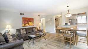 A living room with a sofa, coffee table, and dining area with chairs and a table. - Cradle of Condos ⛳️-  2 Bedroom Pinehurst Getaway (Pinehurst)