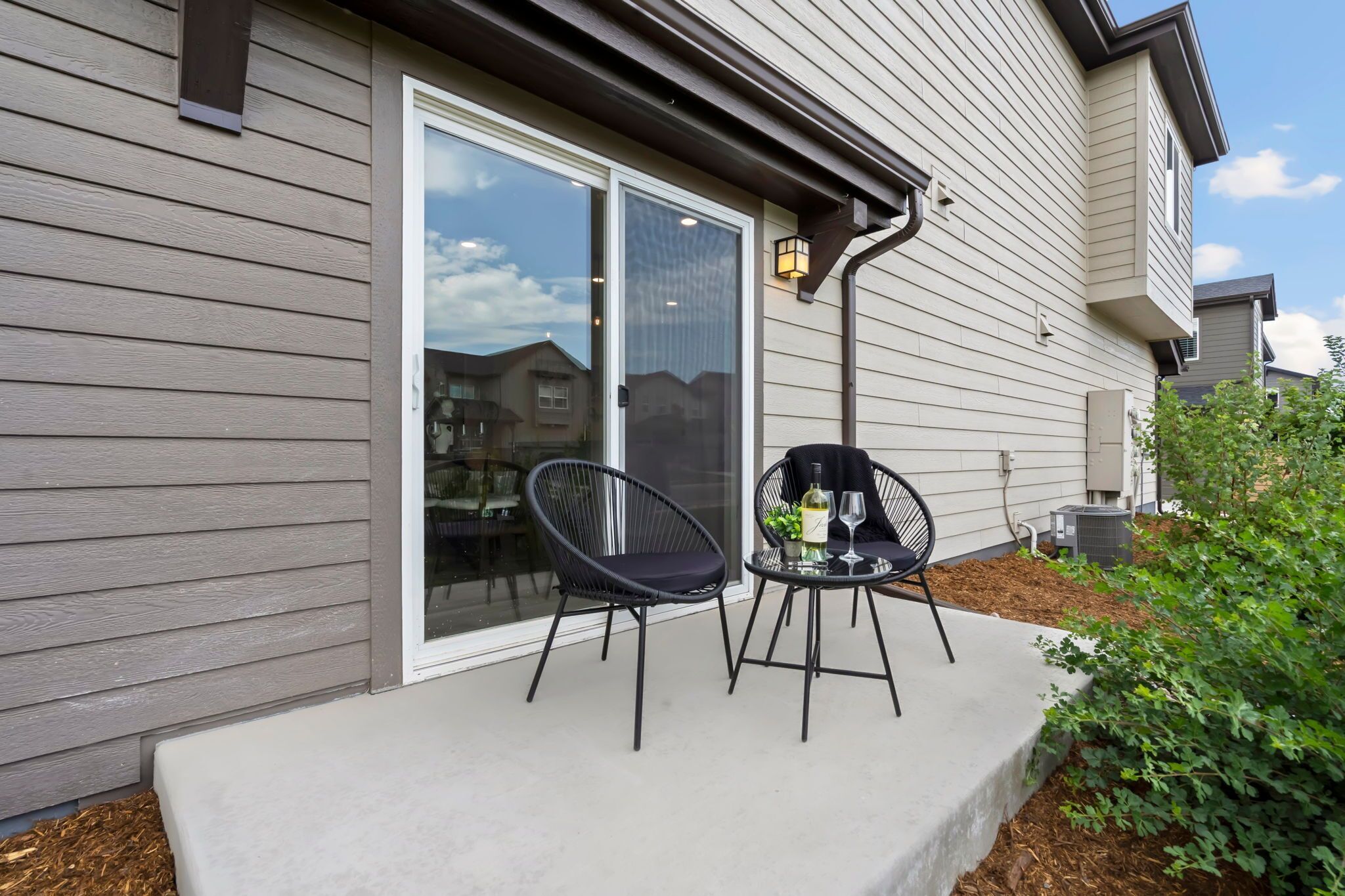 Une maison dotée d’une porte-fenêtre coulissante, d’un petit patio avec deux chaises et une table, et d’un appareil de climatisation visible.