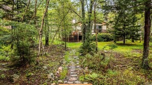 A forested path leading to a cabin with a wooden deck and a stone staircase.