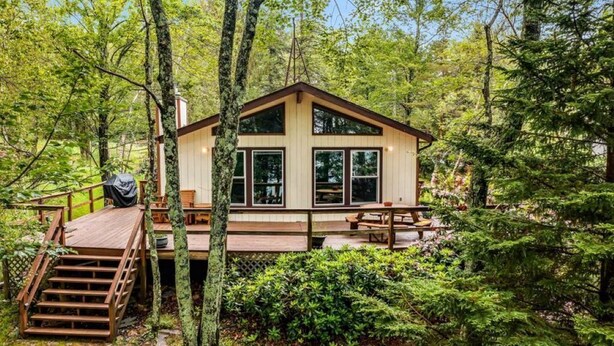 A cabin with a deck, surrounded by dense forest.