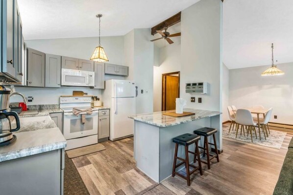 A modern kitchen with grey cabinets, a central island with stools, a microwave, and a refrigerator. - Hot Tub! Lakefront, Firepit, Fireplace, Pet Friendly! (Tobyhanna)