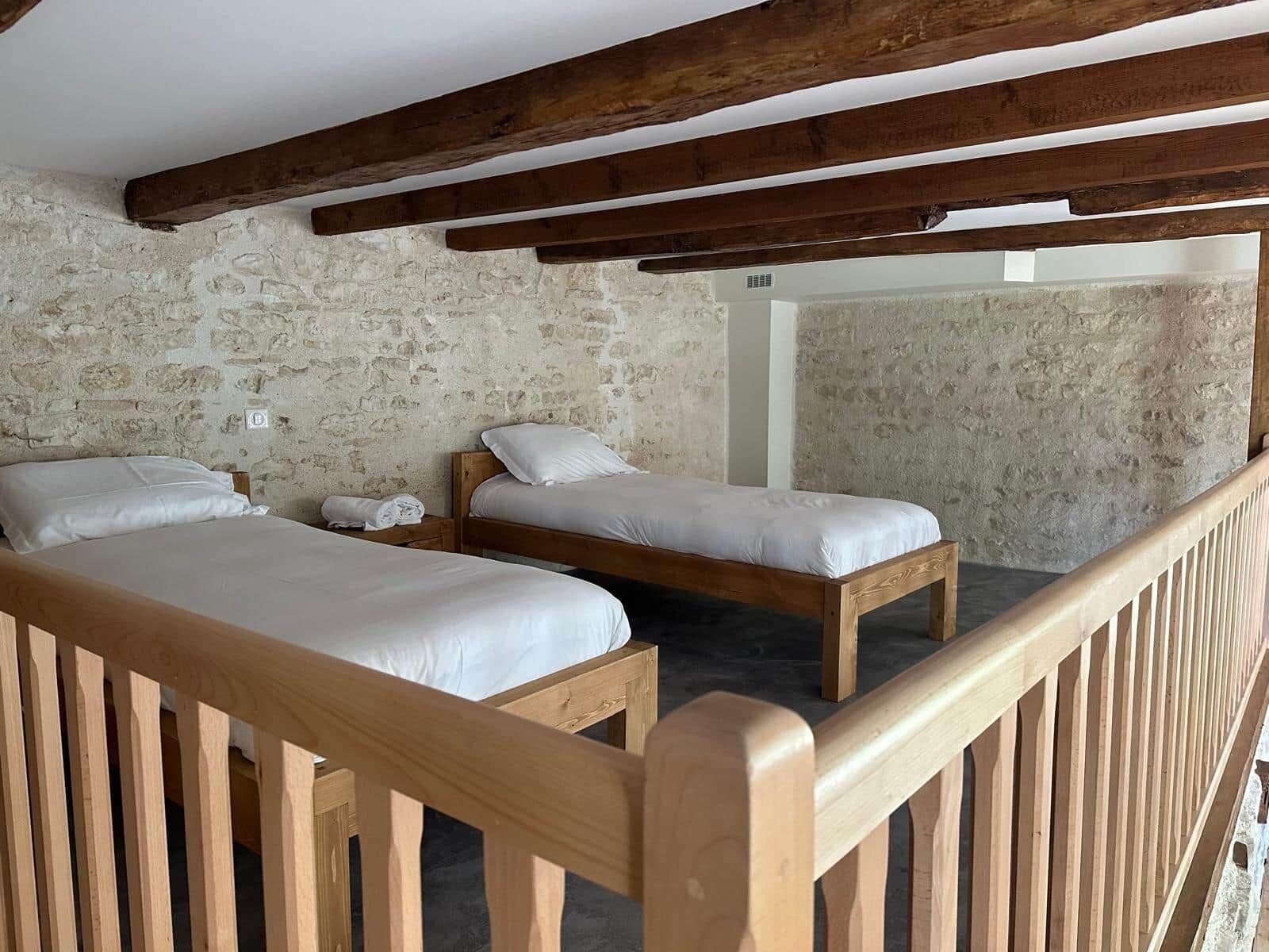 Una habitación con dos camas de madera, una pared de piedra y una barandilla de madera.
