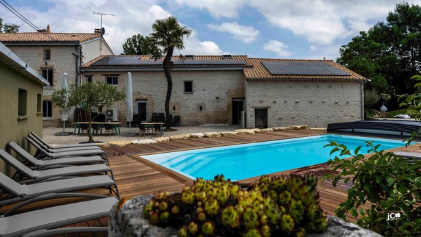 A pool area with lounge chairs, a brick building, and a palm tree. - Le Petit Courault, authenticity and charm (Pamproux)