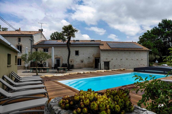 A pool area with lounge chairs, a brick building, and a palm tree. - Le Petit Courault, authenticity and charm (Pamproux)