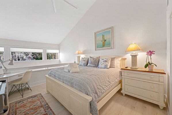 Een slaapkamer met een bed, bureau, stoel, dressoir en een raam met jaloezieën.
