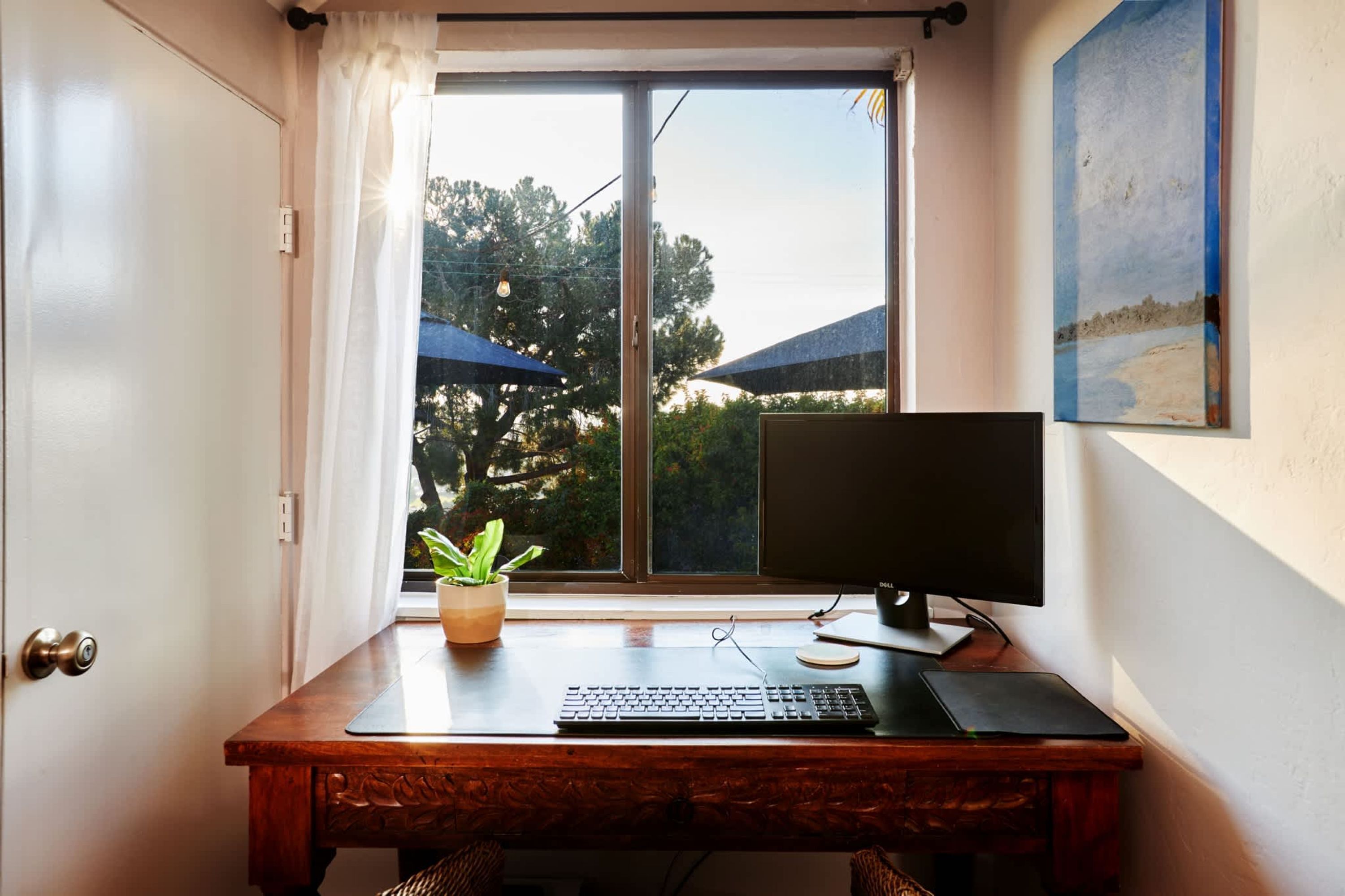 Un bureau en bois avec un écran d’ordinateur, un clavier et une plante en pot.