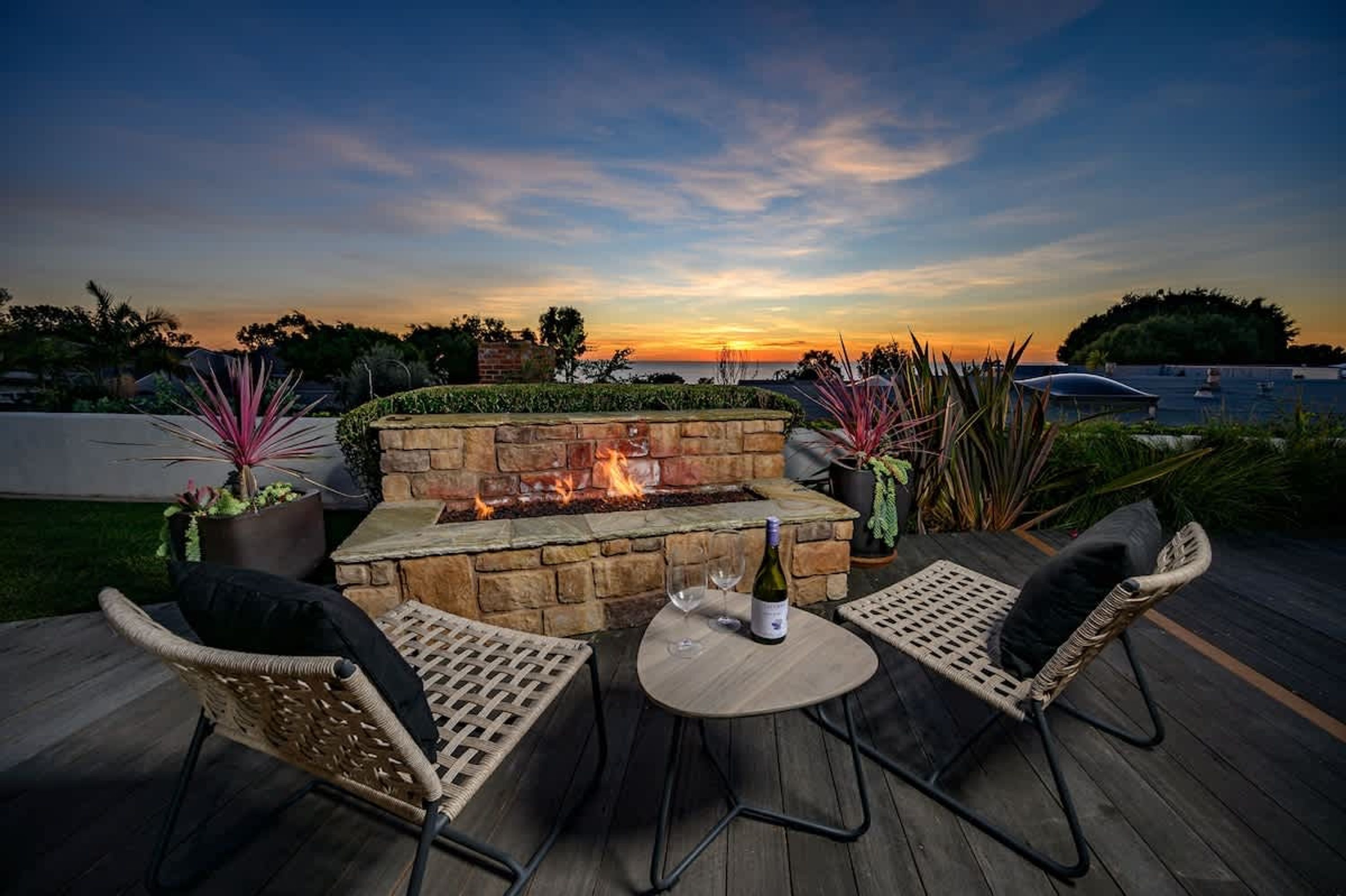 An outdoor patio with a stone fire feature, wicker chairs, and a bottle of wine.