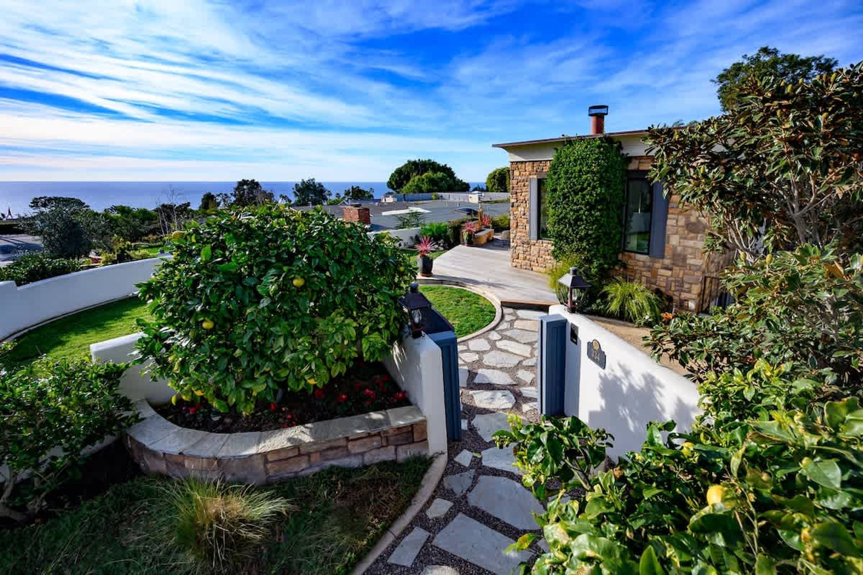 A landscaped garden with a stone pathway, a large bush, and a stone building with a chimney.