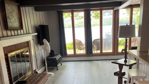 A room with a fireplace, large windows, a wooden floor, and a television.