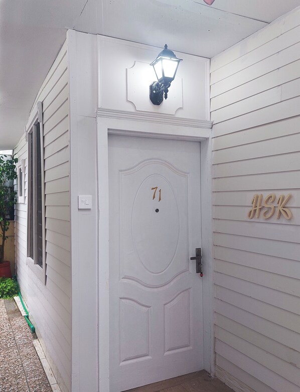A white door with the number 71, a small light fixture above it, and a wooden sign with letters on the wall to the right.