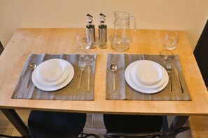 Mesa para comer dispuesta con dos platos, cubiertos, vasos y una jarra.