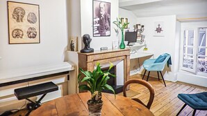 Une pièce comprenant une table à manger en bois, un banc, une plante verte, un buste, un tableau encadré, un ordinateur et une chaise bleue.