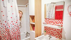 Une salle de bain avec une baignoire, un lavabo et un miroir. Il y a un rideau de douche orné d’un motif de carrés rouges et gris.