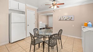 A dining area with a glass table and chairs, a ceiling fan, and a refrigerator.