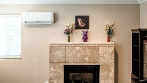 A living room with a fireplace, a mounted air conditioner, and decorative items on the mantel.