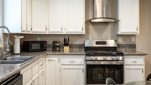 A kitchen with white cabinets, a stainless steel range hood, a microwave, a stove, and a sink.