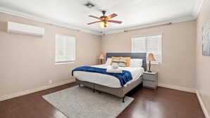 A bedroom with a bed, nightstands, a ceiling fan, and two windows with blinds.