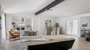 A spacious living area with a sofa, armchair, and a coffee table. There is a kitchen in the background with white cabinets and a microwave. - The Belvedere Pet Friendly Spacious Yard (Plano)