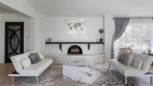 A living room with a white brick fireplace, two white sofas, a marble coffee table, and a world map artwork on the wall. - The Belvedere Pet Friendly Spacious Yard (Plano)
