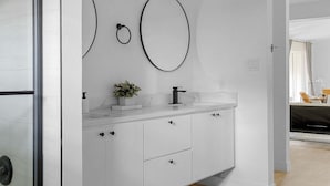 A modern bathroom with white cabinetry, a marble countertop, and a large mirror with two circular frames. - The Belvedere Pet Friendly Spacious Yard (Plano)