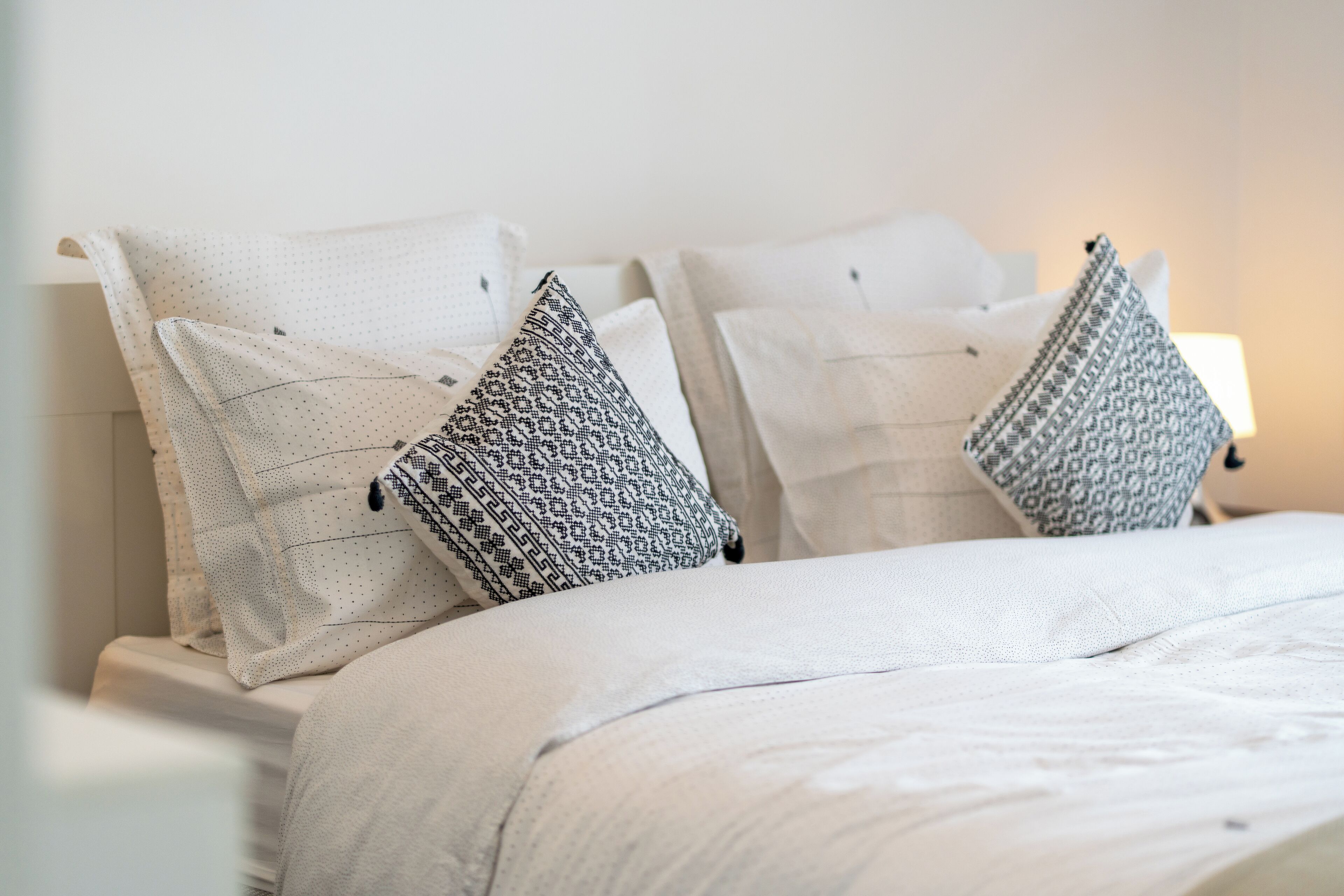 A neatly made bed with white bedding and two patterned pillows.